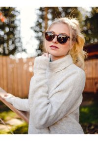 Světlý šedý rolák s žebrovanými manžetami, doplněný kulatými slunečními brýlemi s želvovinovým vzorem a světlými blond vlasy staženými do ohonu.