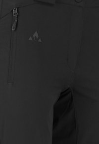 Pantalons softshell noirs avec une poche zippée et un détail de logo. Le matériau est lisse avec une finition mate et un design épuré.