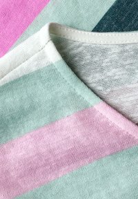 Páskovaný textil v zelených, růžových a šedých odstínech, s měkkou texturou. Design s výstřihem do V a kontrastními švy na výstřihu.