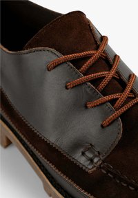 Zapato de cuero marrón y gamuza con cordones, que presenta un upper suave, costuras contrastantes y cordones trenzados. La suela gruesa añade durabilidad.