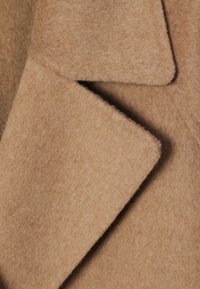 Kappaull i camel med en mjuk, texturerad finish, med en ren slagdesign och överlappande kragekanter.
