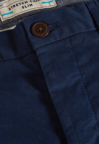 Chinos en azul marino elástico con una textura suave, que cuentan con un botón marrón en la cintura y una etiqueta que dice "STRETCH CHINOS SLIM."