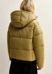 Chaqueta acolchada color verde oliva con capucha, que presenta un diseño acolchado y costuras horizontales. Parece estar aislada con un acabado suave.