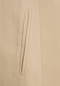Tessuto beige con una superficie testurizzata presenta una tasca verticale. Il design è semplice e funzionale, enfatizzando il minimalismo.