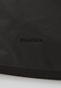 Zwarte nylon draagtas met een gestructureerd oppervlak en een verdiept "Marc O'Polo" logo. Eenvoudig ontwerp zonder zichtbare bevestigingsmiddelen of accents.