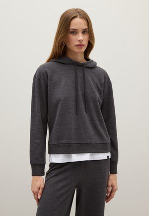 Sweatshirt à capuche gris foncé avec des poignets et un ourlet côtelés, à la coupe décontractée et avec un cordon de serrage ajustable. Superposé à une chemise blanche.