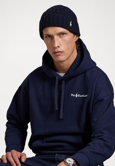 Temno modra kapuca z sprednjim žepom in vrvico, ki vključuje belo logotip "Polo Ralph Lauren". Rebrast pletena temno modra zimska kapa z logotipom.