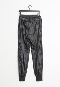 Svarta träningbyxor i en glänsande, texturerad kvalitet. Smalnande ben med elastiska muddar och en åtsittande midja. Detaljer på baksidan.