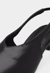 Μαύρο δερμάτινο παπούτσι με λουράκι πίσω, με χαμηλό τετράγωνο τακούνι και μυτερή μύτη, εμφανιζόμενο από κοντινή γωνία.