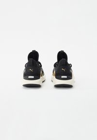 Sorte træningssko med guld detaljer, mesh-overdel, polstret krave og kontrasterende cremefarvet sål. Har Puma-logo på hælen.
