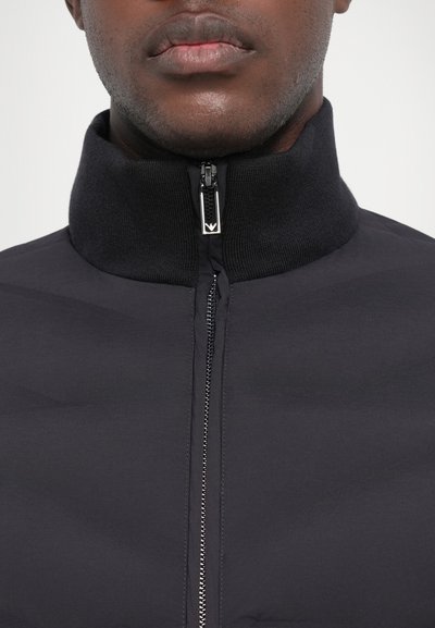 Black jacket with a high collar, featuring a front zipper and textured knit accents. Smooth fabric with a sleek, minimalist design.