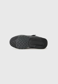 Semelle de chaussure de sport noire avec caoutchouc texturé pour l'adhérence, présentant un motif de bande de roulement et une section lisse près du talon pour la stabilité.