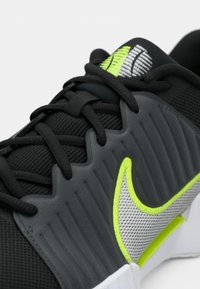 Μαύρο αθλητικό παπούτσι με υλικό από υφασμένο δίχτυ, ανακλαστικές γκρι λεπτομέρειες, λογότυπο σε νεον πράσινο και λαστιχένια σόλα με ανάγλυφο σχέδιο.