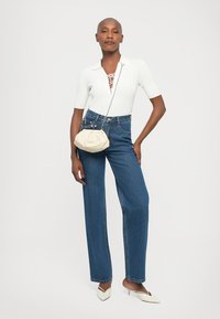White knit top with a collared neck, blue high-waisted jeans, and a cream-colored shoulder bag. Model wearing white heeled mules.