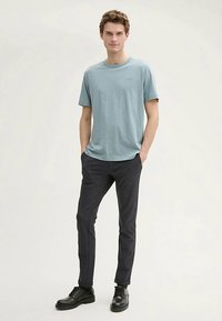 Világoskék rövid ujjú póló sötét, texturált nadrággal és fekete fűzős csizmával párosítva. Egyszerű dizájn, laza szabás, minimális márkajelzés látható.