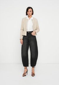 Μπεζ σακάκι πεπλούμ πάνω από λευκό πουκάμισο, συνδυασμένο με μαύρο τζιν ψηλόμεσο. Μαύρα πέδιλα με λουράκια ολοκληρώνουν το σύνολο. Απλός και καθαρός σχεδιασμός.