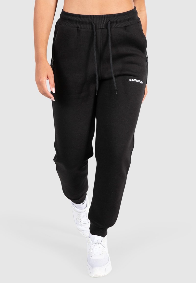 Svarta sweatpants med snörning i midjan, sidofickor med dragkedja och en liten vit logotyp. Tillverkade av mjukt, strukturerat tyg med en avslappnad passform.