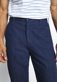 Tummansiniset puuvillahousut suoralla lahkeella, joissa on nappisuljenta ja sivutaskut, sileä tekstuuri ja ilman näkyviä kuvioita.