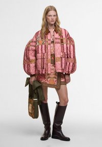 Ραμμένο ροζ σακάκι με φουσκωτά μανίκια, κεντημένα λουλούδια, συνδυασμένο με ένα μοτίβο μίνι φόρεμα, πράσινη τσάντα και καφέ μπότες μέχρι το γόνατο.