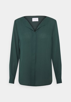 Blouse femme à manches longues de couleur vert foncé, col en V et boutons dissimulés à l'avant, présentée sur un fond clair uni.