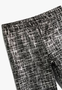 Leggings con estampado en blanco y negro con una tela texturizada, que presentan una cinturilla elástica ancha y un diseño geométrico en forma de cuadrícula.