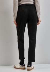 Zwarte suède-achtige broeken met een taps toelopende pasvorm, elastische tailleband en twee achterzakken, gecombineerd met witte en beige sneakers.