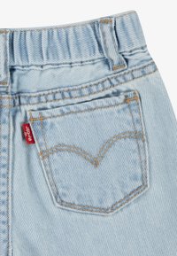 Lysblå denimjeans med en syet baglomme med et karakteristisk buet design og et lille rødt mærke.