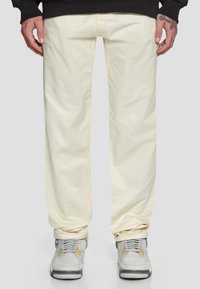 Beige bomullsbukser med avslappet passform, med subtile sømdetaljer. Kombinert med grå sneakers med gule accenter.