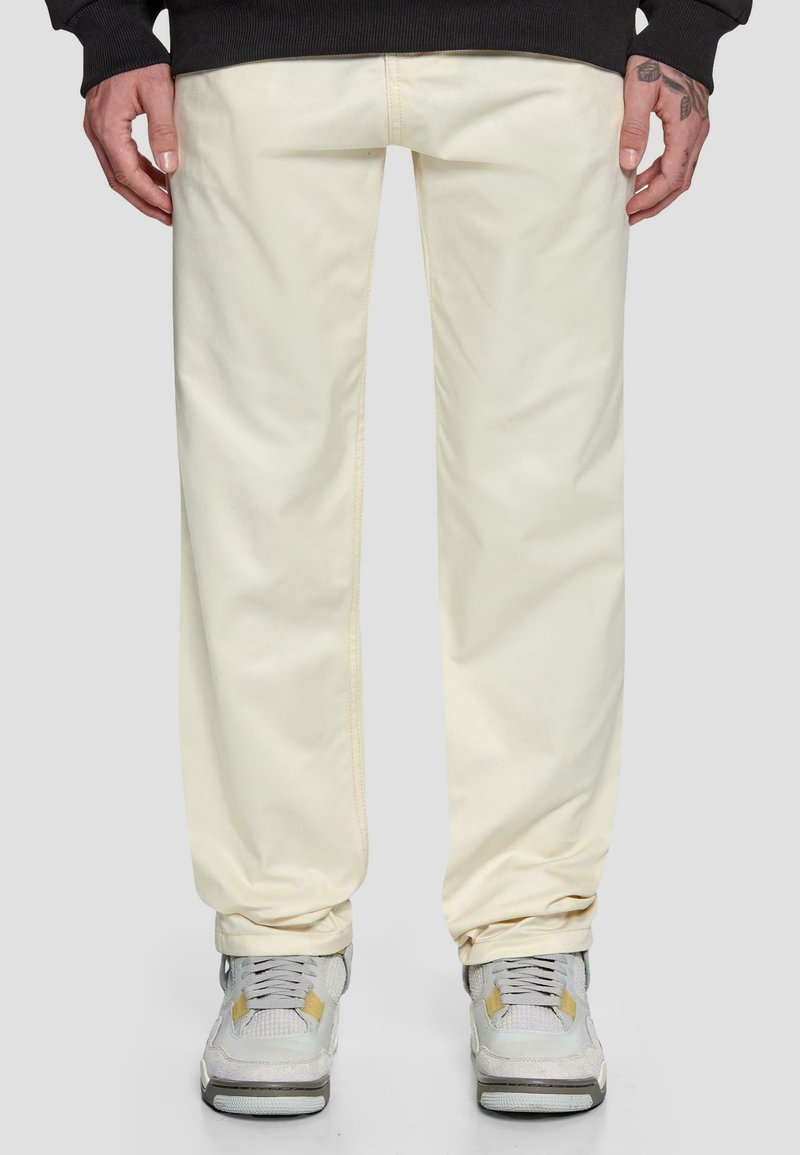 Beige bomullsbukser med avslappet passform, med subtile sømdetaljer. Kombinert med grå sneakers med gule accenter.