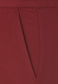 Nahaufnahme von tief rotem Stoff mit einer genähten schrägen Tasche und detaillierten Nähten entlang der Naht.
