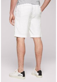 Shorts en lin blanc avec une coupe décontractée, dotés d'une ceinture et de deux poches arrière. Portés avec des baskets blanches, agrémentées d'un détail noir au talon.