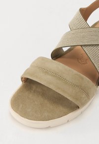 Beige semskede sandal med kryssmønstrede tekstilstropper og en lys gummisåle. Oversiden har en jevn overflate og subtil søm.