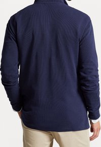 Camisa polo de manga larga en azul marino con cuello, tejido texturizado y un corte relajado, que cuenta con un dobladillo redondeado y puños en las muñecas.