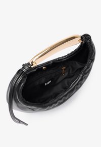 Melnā ādas soma ar zelta tonī metāla rokturi, pievilkts dizains, mīksta tekstūra un oderēta iekšpuse ar lietusvārdu kabatu.