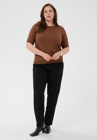 Haut marron à manches courtes avec un col rond, associé à un pantalon noir sur mesure et des bottines à talons noires. Design simple et ajusté.