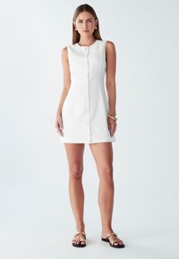 Biela mini šaty bez rukávov s okrúhlym výstrihom, predným zapínaním na gombíky a priliehavým strihom. Hladká tkanina a minimalistický dizajn.