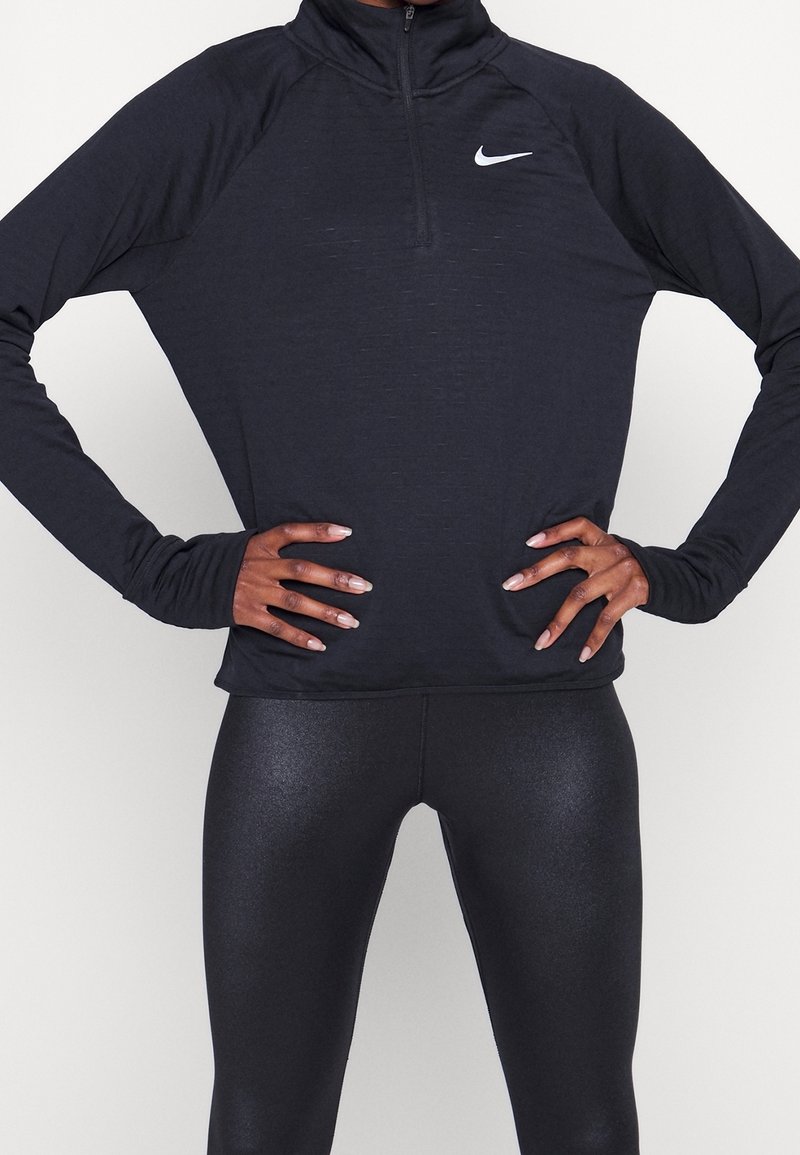Zwarte, langmouwige Nike-top met een kwart rits, voorzien van een subtiel textuurpatroon. Gecombineerd met glanzende zwarte leggings.