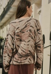 Pulover cu un model roz și bej, realizat dintr-un material moale și texturat, având desene abstracte în culori închise și o croială lejeră, purtat peste o fustă lungă.