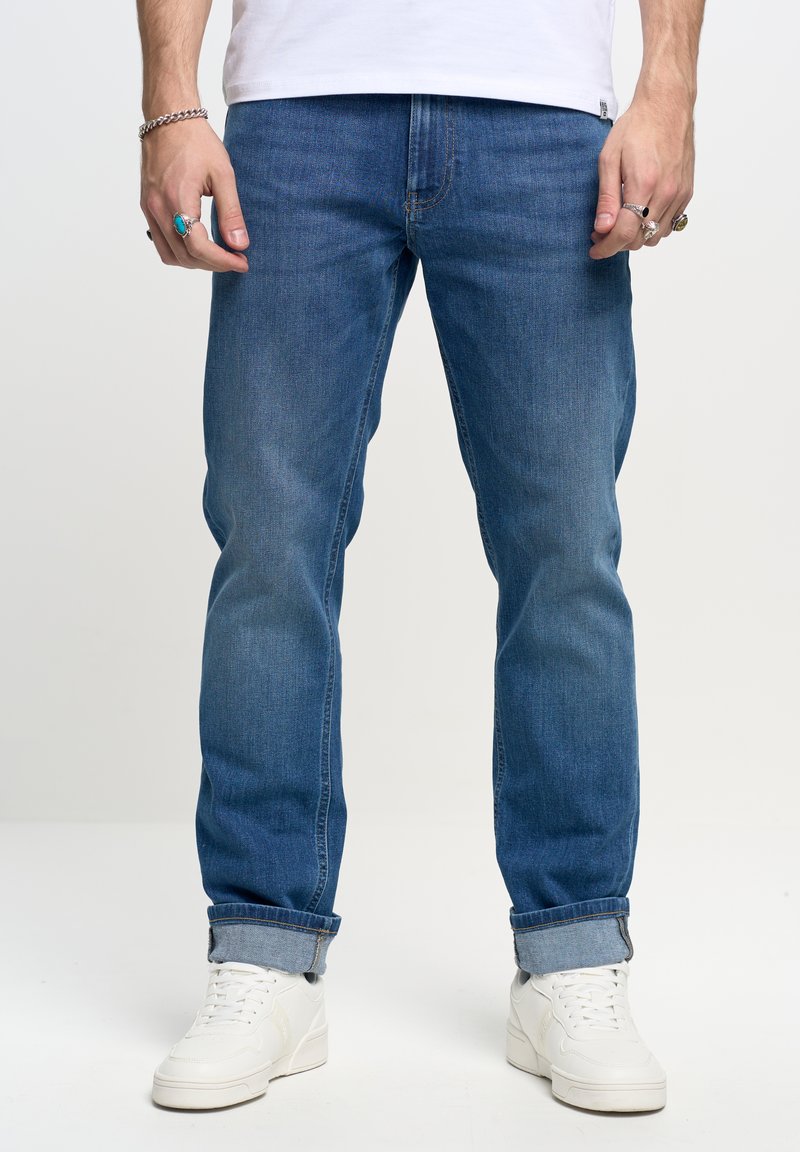 Jeans in denim blu con taglio dritto, caratterizzati da una finitura leggermente sbiadita e orli arrotolati. Abbinati a sneakers bianche.