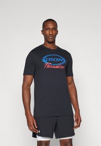 Sort bomulds T-shirt med korte ærmer, der har et blåt og rødt logo med teksten "IRON Paradise" på forsiden, parret med sorte shorts.