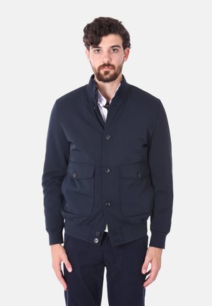 Giacca blu navy realizzata in tessuto liscio, con colletto alto, chiusura frontale con bottoni e due grandi tasche applicate.