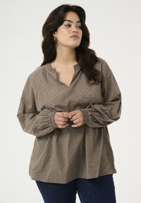 Langarmige, taupe blouse met een notch halslijn, geplooide manchetten en een subtiel textuurpatroon van kleine stippen. Ontspannen pasvorm en zachte stof.