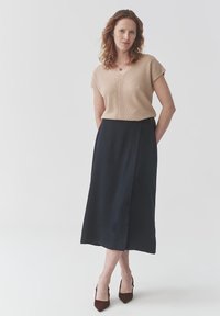 Top de punto acanalado beige con mangas cortas, combinado con una falda midi azul marino con una abertura lateral. Tacones marrones de punta afilada completan el conjunto.