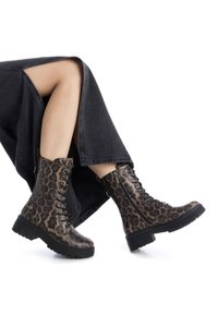 Botas de combate con estampado de leopardo y suelas negras, diseño con cordones, cremalleras laterales y superficies texturizadas, combinadas con una falda gris.