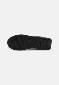 Zwarte rubberen sneakerzool met diepe groeven en het geperste logo "HUGO." Getextureerd oppervlak voor grip en stabiliteit.