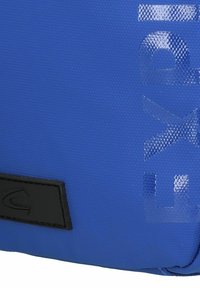 Bolsa de tela azul con una superficie texturizada, con un acento negro y un logo en relieve con un acabado reflectante de luz.