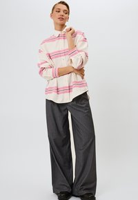 Hvid skjorte med lyserøde og grå striber, knappet fortil, opbrettede ærmer; parret med grå stribede bredbenede bukser og sorte sko.