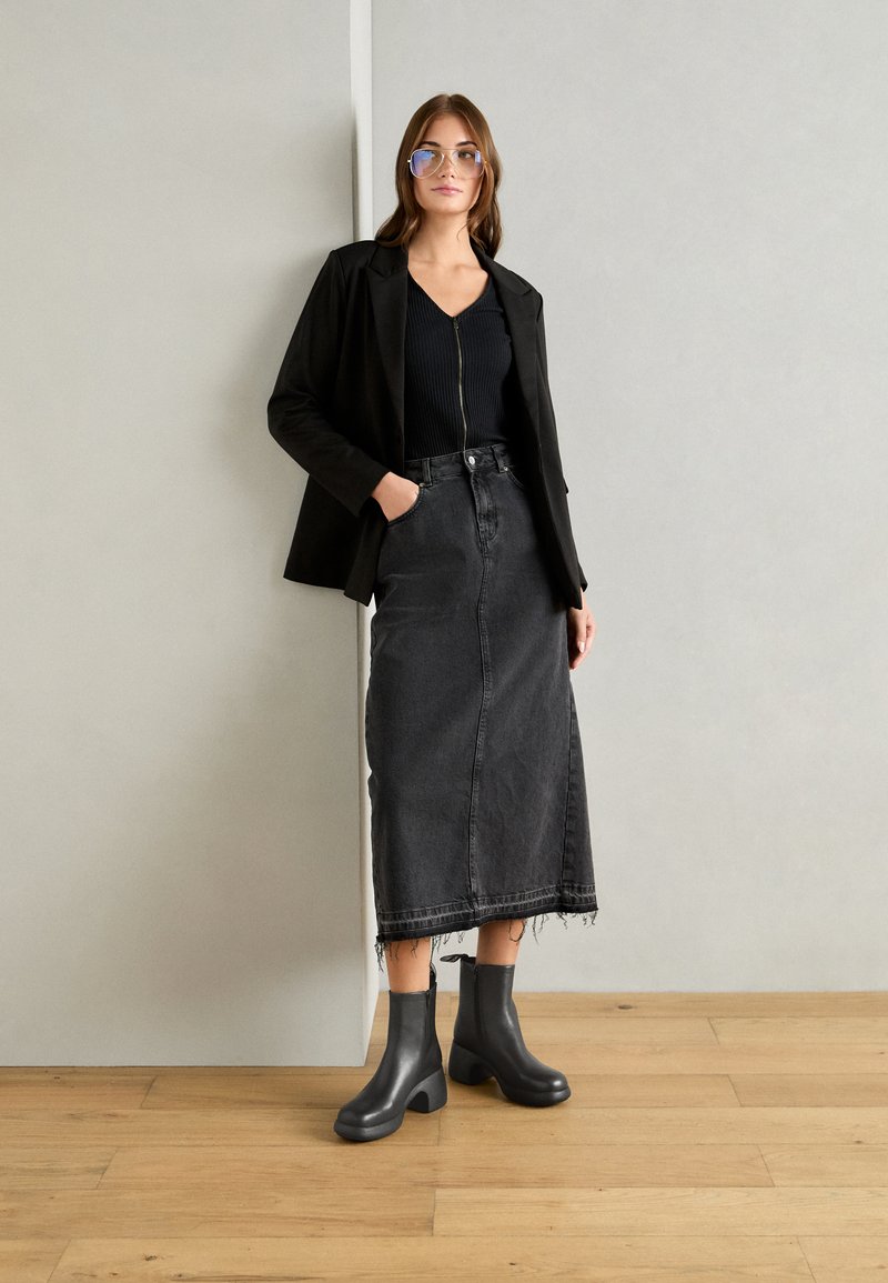 Sort blazer over en sort ribbet top, parret med en højvæltet, mørk denimnederdel og sorte ankelstøvler med en kraftig hæl og rund tå.