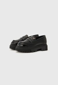 Mustadast nahast loaferid, millel on paksu platvormi tald, horisontaalsed rihmade aksendid ja väike kuldne logo detail külgedel.