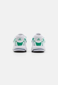 Scarpe sportive bianche con dettagli verdi, dotate di una tomaia in rete, suola imbottita e logo Adidas ben visibile sul tallone.